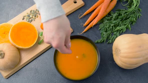 Hand Adding Pumpkin Seeds and Mint Leaf To Soup 