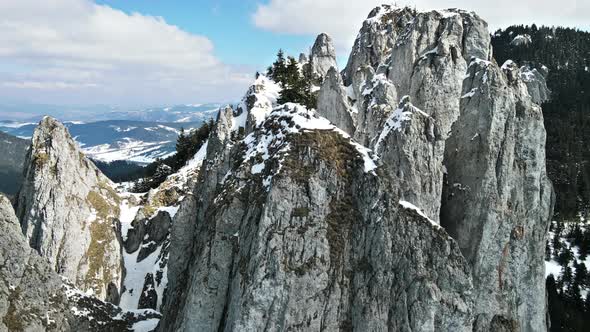 Aerial drone view of the spring Carpathians, Romania. Rocky peak with cross, valleys partly covered 