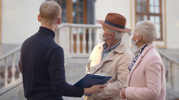 Male Real Estate Agent and Senior Couple in Safety Mask Discussing Over Documents Outdoors