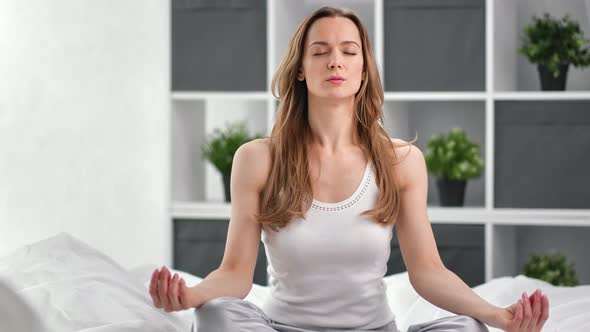 Relaxed Woman Meditating Sitting in Lotus Position on Bed