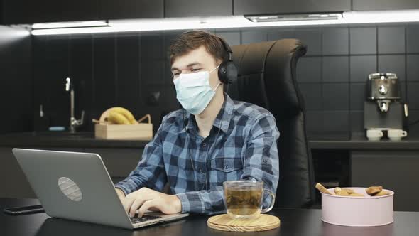 Man in protective medical face mask making video call conference from home workplace. 