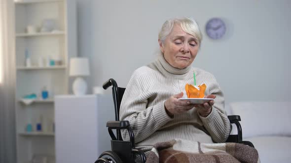 Crying Old Woman in Wheelchair Blowing Out Candle on Cake and Looking at Camera