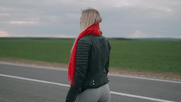 Depressed Blonde Woman Is Walking on the Road. Lonely Girl with a Red Scarf