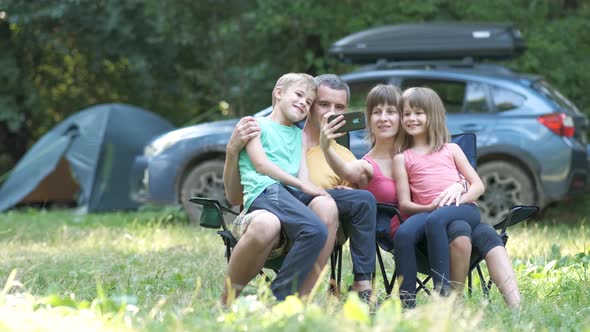 Happy family sitting together at campsite and taking selfie with mobile phone