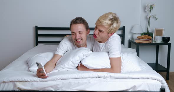 Homosexual Couple Hugging Looking at Smartphone Camera When Making Selfie Photos