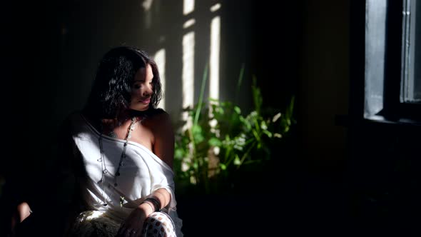 Pretty Tender Brunette is Sitting Alone in Room with Many Houseplants and Bright Sun Rays in Morning