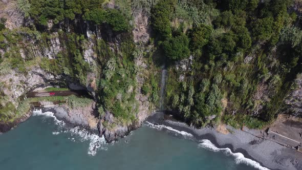 Aerial view of the ocean and cliffs. A car appears from the tunnel.