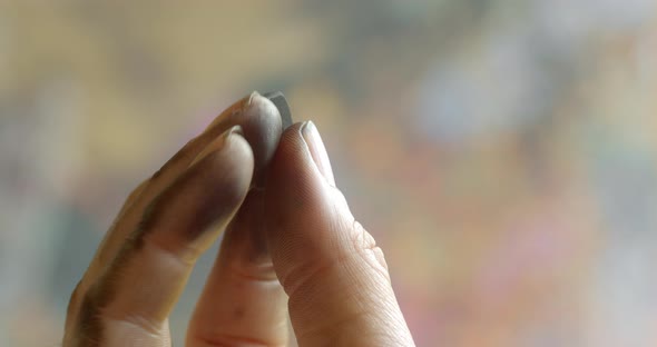 A hand plays with small charcoal on a blurred multicolored background