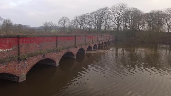 Low panning aerial shot across archway bridge over water