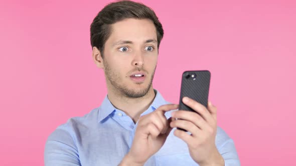 Young Man Celebrating Success While Using Smartphone on Pink Background