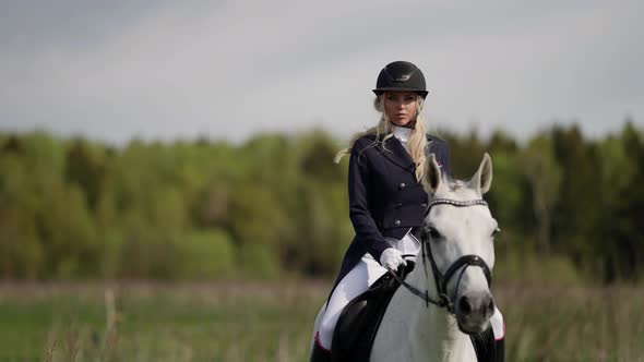 A Female Professional Jockey Riding a White Horse Gallops Across a Field