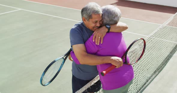 Video of happy biracial senior couple embracing on tennis court