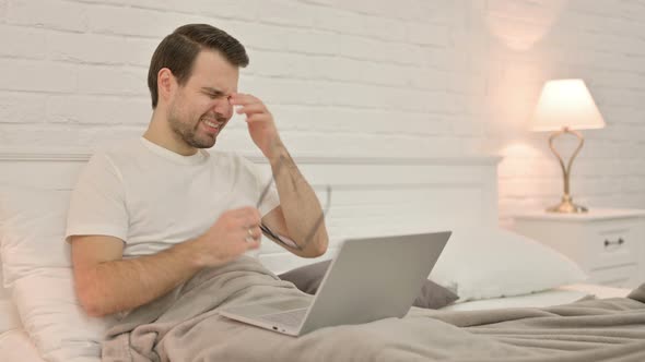 Stressed Young Man with Headache Sitting in Bed