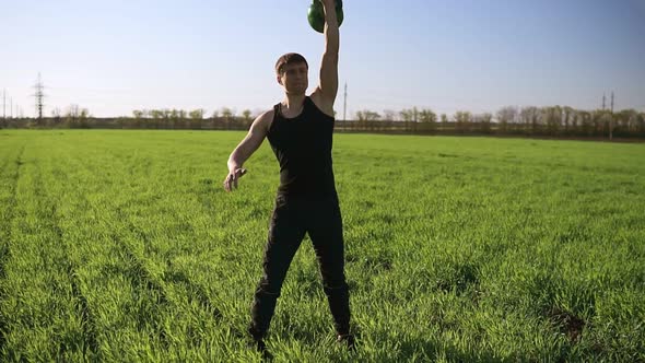 A Young Man with a Sporty Physique Lifts a Weight with One Hand