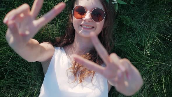 SLOW MOTION: Top view shot of a Caucasian girl in a white floral dress lying in grass and shows a si