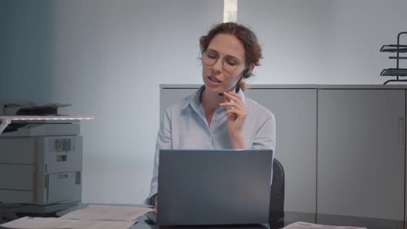 Female Operator in Braces and Headset Talking with Costumer Working on Laptop Computer in Office