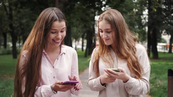 Two charming young girls using mobile phones outdoors. Two beautiful freelance woman.
