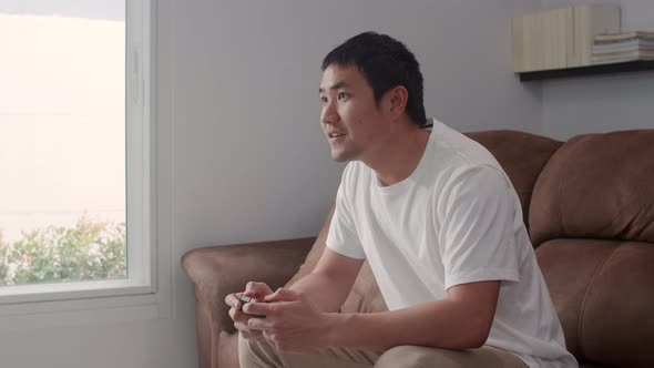 Young Asian man using joystick playing video games in television in living room