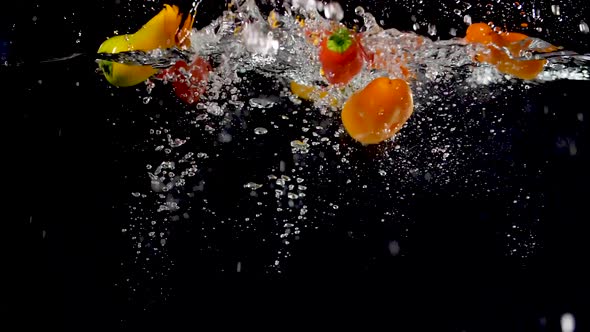 Vibrant sweet peppers being dropped into water in slow motion.