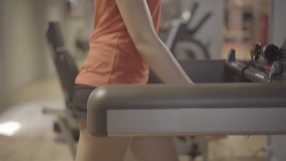 Camera Moves Up Along Slim Body of Beautiful Young Caucasian Woman Walking on Treadmill. Side View