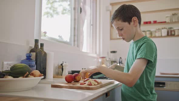 Young boy working in the kitchen slicing fruit for breakfast