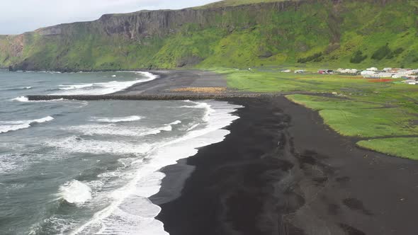 Black sand beach with waves in Vik, Iceland with drone video moving down.