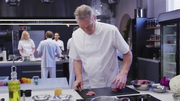 Professional Caucasian male chef wearing chefs whites in a restaurant kitchen slicing meat on a cutt
