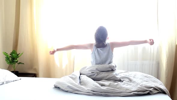 child sits on the bed in the bedroom and stretches after waking up in the morning