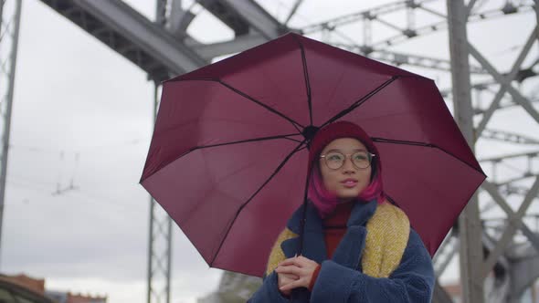 Cheerful Asian Woman Walking with Umbrella on Urban Bridge