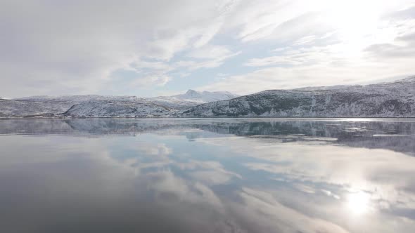 Calm Fjord Sea Water Mirroring Snowy Mountain Slope And Sky In Norway