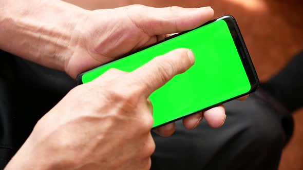 Close-up of an old man's hand using a smartphone with a green screen chroma key