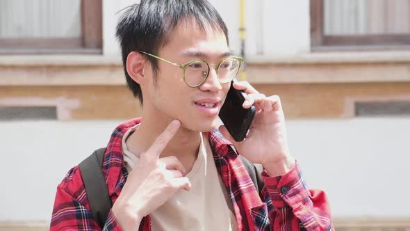 Asian Man Holding Smartphone and Talking By Phone with Friend Smiling and Laughing Outdoor