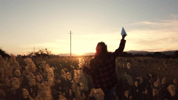 Traveling woman with paper airplane enjoying life and freedom at the land at sunset.