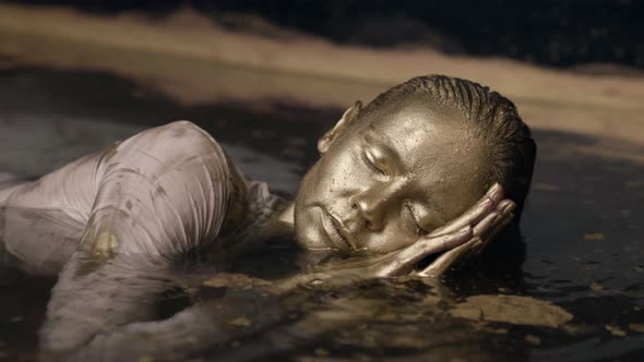 The Woman's Face is Lying in the Water All Covered with Gold Paint