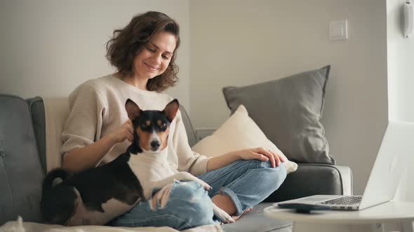 A Young Woman Working on a Laptop While Sitting on a Sofa with Her Cute Dog