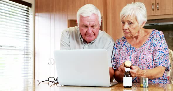 Senior couple checking medicine while using laptop in kitchen