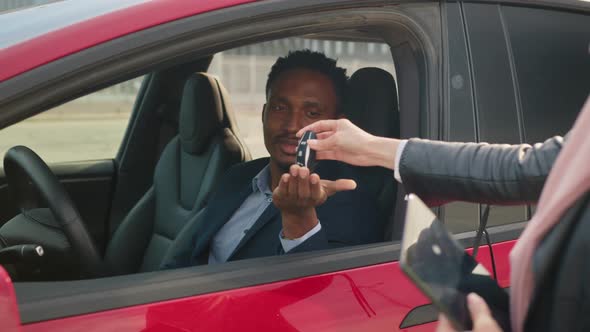 Happy African Man Sitting Inside His New Electric Car While Taking Keys From