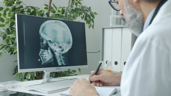Doctor Radiologist Analyzing Human Skull Images Looking at Computer Screen and Witing Indoors in