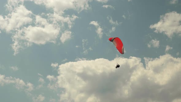 Paraglider flying with red parachute on background of sun and beautiful clouds.