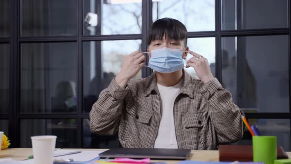 Asian Man Posing in Medical Mask at Workstation