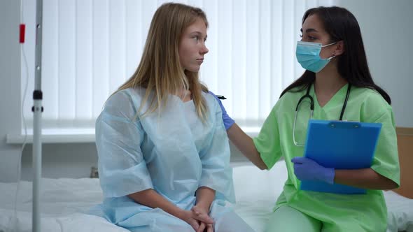 Portrait of Devastated Teenage Girl Sitting on Bed in Ward with Doctor Supporting Patient