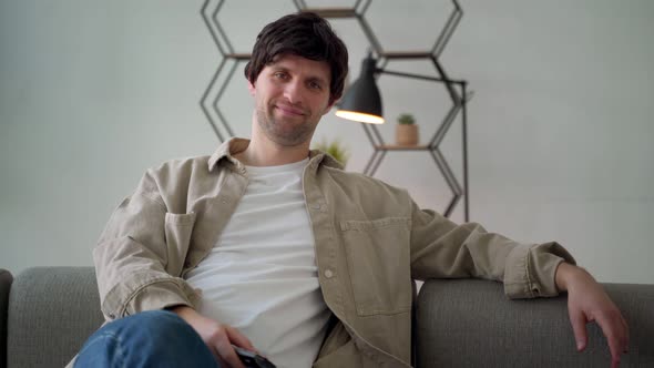 A Smiling Man with a TV Remote Control at Home Watching TV Sitting on the Couch