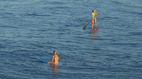 A young woman SUP surfing in a bikini on a stand-up paddleboard surfboard.