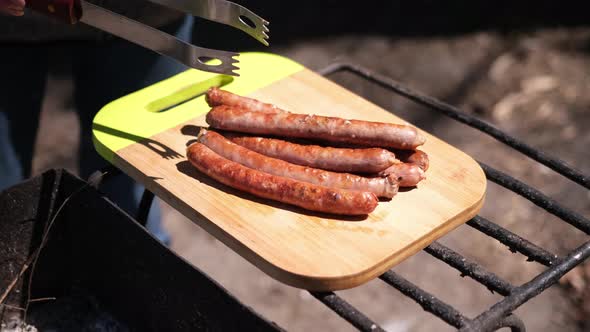 Puttung Tasty Grilled Sausages on a Wooden Cutting Board