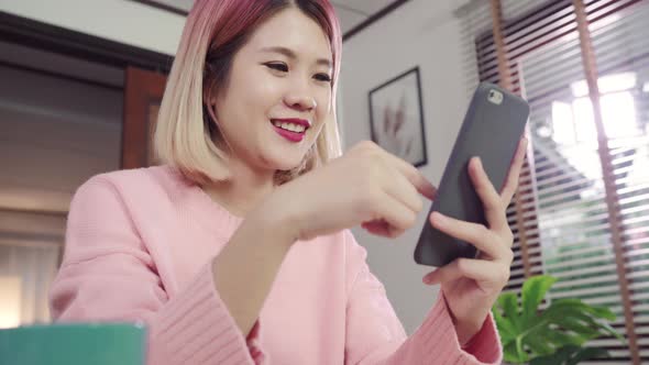 Young Asian woman using smartphone while lying on the desk in her living room