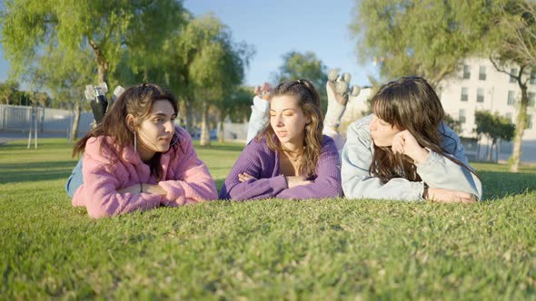 Girls with Rollerskates Lie on Grass in Sunlight and Chat Ground View