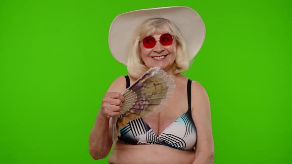 Senior Old Woman Tourist Exhales From Heat or Stuffiness Waves Hand Fan at Herself on Chroma Key