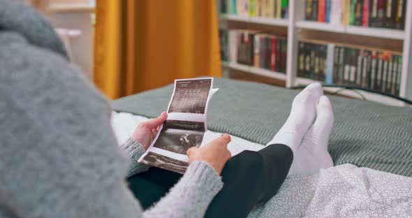 Video of Beautiful Young Pregnant Woman Looking Ultrasound Prints While Lying on Bed