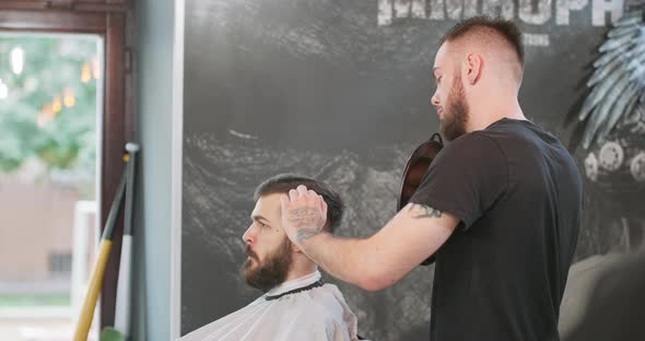 Male Barber with Mirror in Hands Stays Behind the Client Shows the Result of His Work to Young Man