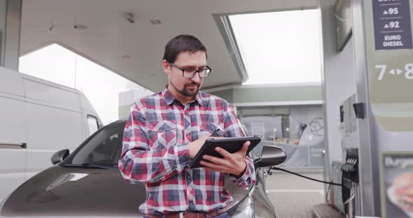 Young Handsome Caucasian Man Standing in Front of His Car and Working on Tablet